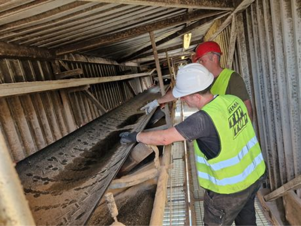 Two REMA TIP TOP employees in a shaft point to a conveyor belt
